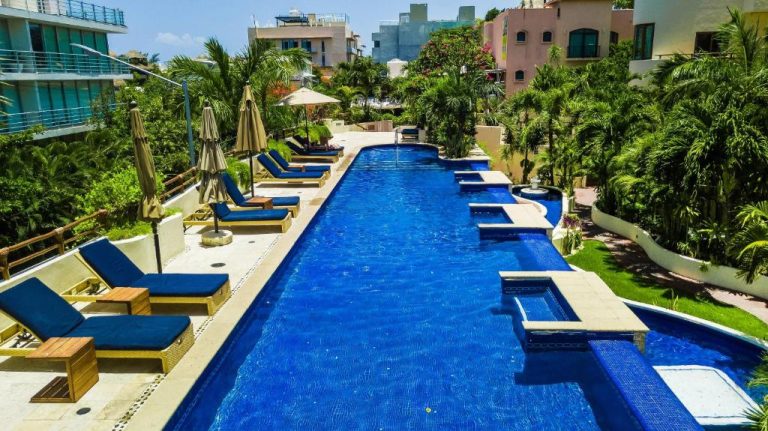 Piscina exterior alargada con tumbonas azules y jacuzzi del Porto Playa Condo Hotel and Beach Club