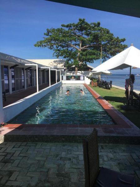 Piscina exterior alargada con vistas al mar en The Beachhouse Cebu, rodeada de jardín tropical