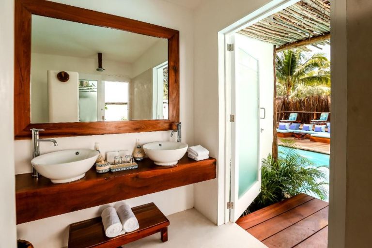 Baño doble con lavabos en madera y acceso directo a la piscina exterior en Cabanas Tulum Beach Hotel & Spa