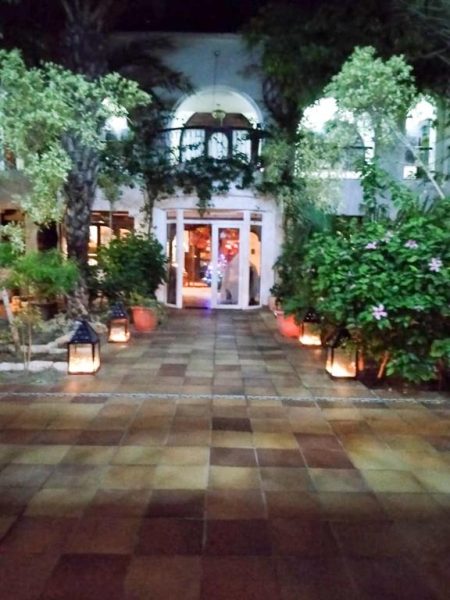 Entrada principal iluminada con faroles del Hotel Dar El Bhar rodeada de jardines y vegetación mediterránea de noche