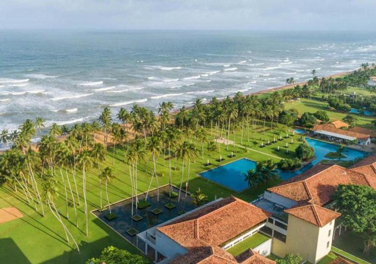 Vista aérea de las piscinas exteriores y jardines tropicales del The Blue Water Geoffrey Bawa Heritage Resort frente al mar
