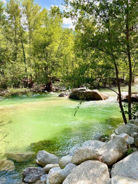 Río de aguas cristalinas verdes con rocas y vegetación natural del Appart'Hotel Castel Emeraude
