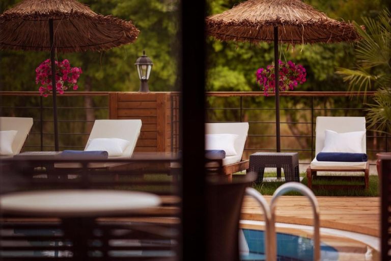 Terraza con tumbonas blancas y sombrillas de paja junto a la piscina del Arwen Hotel