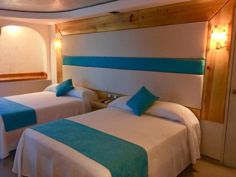 Habitación doble con camas blancas y detalles en azul turquesa en Hotel Blue Star Cancun