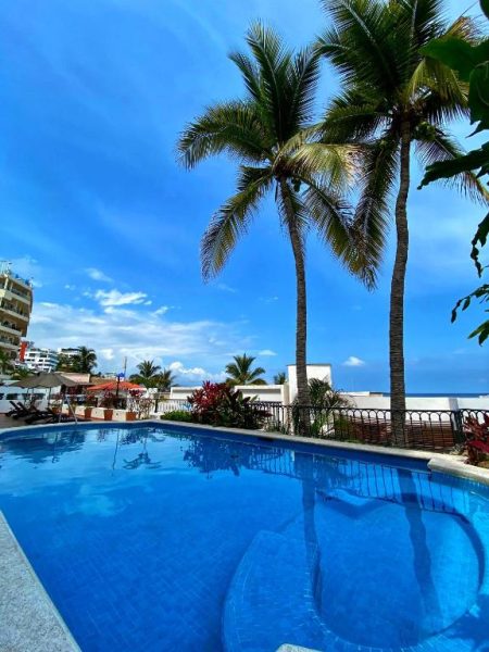 Piscina exterior con palmeras tropicales y vista al mar en One Beach Street Zona Romántica Puerto Vallarta