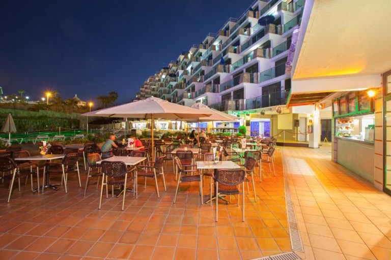 Terraza exterior del restaurante Grupotel Revoli iluminada de noche con mesas y sombrillas
