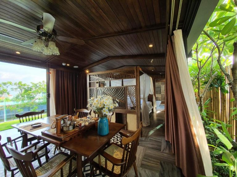 Suite con comedor de madera y cama con dosel en Minh Boutique, rodeada de jardín tropical