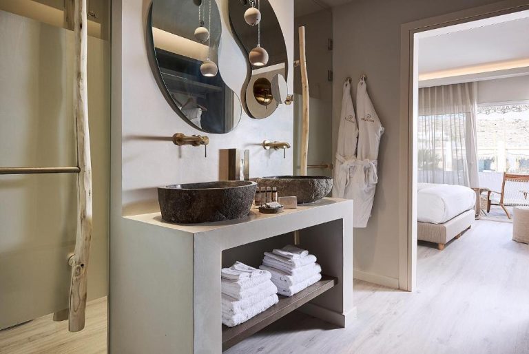 Baño de lujo con lavabos de piedra natural y espejos redondos en Palladium Hotel