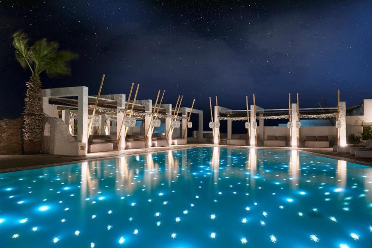 Piscina iluminada de noche con luces azules y cielo estrellado en Palladium Hotel