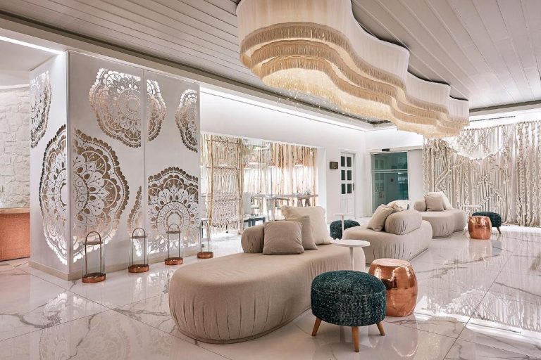 Elegante lobby del Palladium Hotel con sofás blancos, araña de flecos y paneles decorativos con mandalas