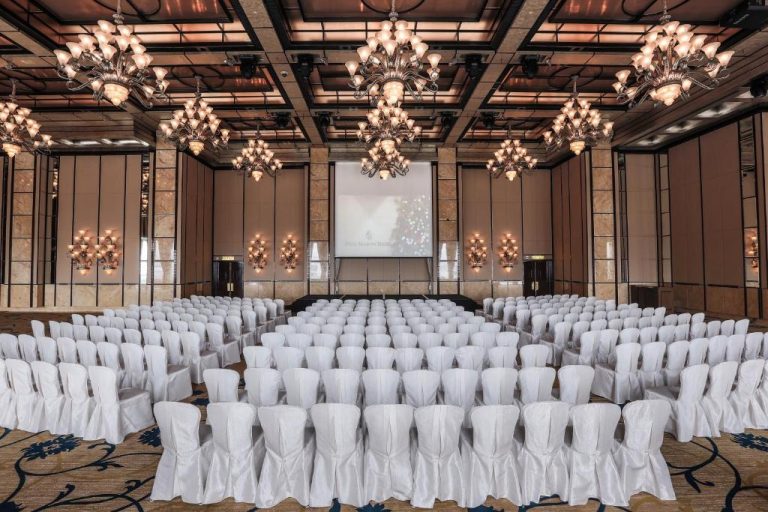 Salón de conferencias y banquetes con sillas blancas y lujosas arañas de cristal en Four Seasons Hotel Hong Kong