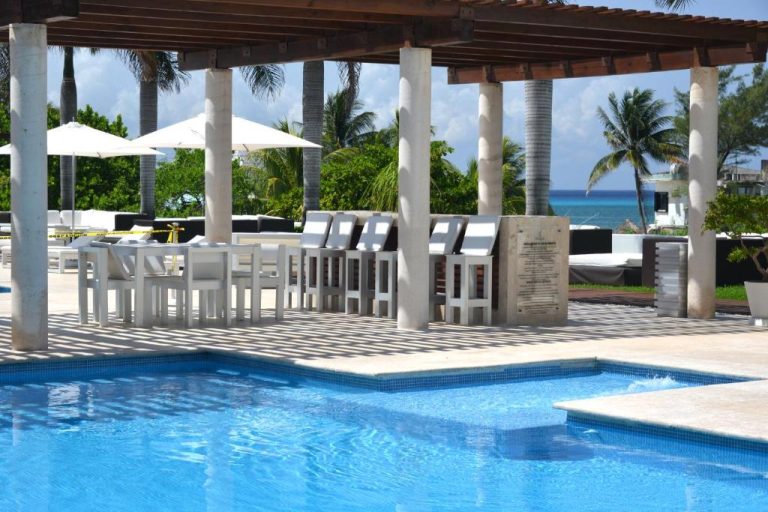 Piscina exterior con bar y tumbonas blancas en Magia Beachside Condo con vistas al mar Caribe