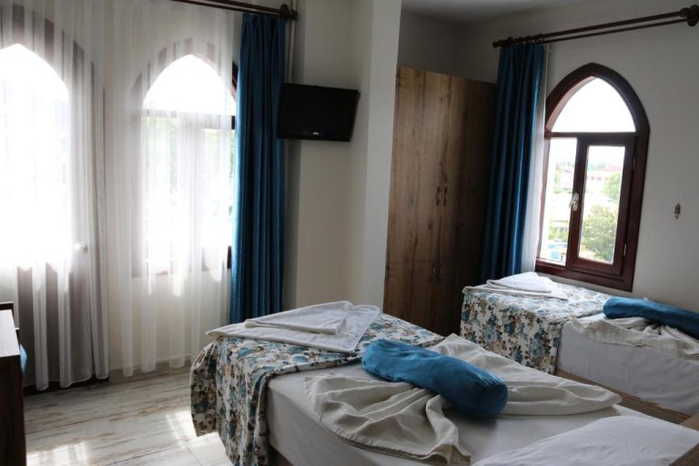 Habitación doble con dos camas individuales y ventanas con cortinas azules en Eroglu City Hotel