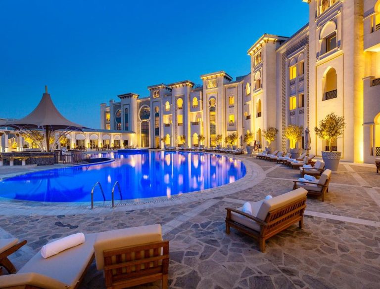 Piscina exterior iluminada al atardecer del Ezdan Palace Hotel con arquitectura árabe y tumbonas
