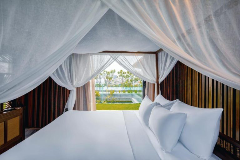 Habitación con cama dosel y cortinas blancas con vistas al jardín y piscina en Minh Boutique
