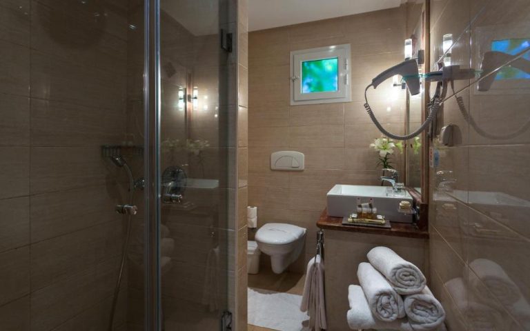Baño moderno con ducha de cristal, lavabo y toallas blancas en The Sindbad Hotel