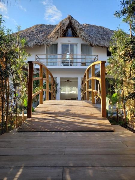Pasarela de madera con arcos que da acceso al Takuma Boutik Hotel con techo de palapa y balcón