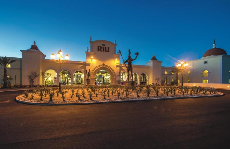 Entrada principal iluminada del Riu Palace Cabo San Lucas All Inclusive con estatua y jardines de noche
