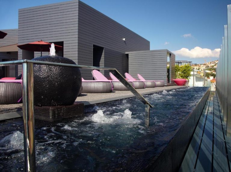 Piscina infinita con fuente decorativa y tumbonas rosas en la terraza del The Vine Hotel