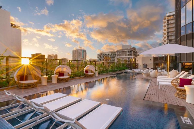 Piscina en la azotea del Hyatt Centric Waikiki Beach con tumbonas y vistas a la ciudad al atardecer