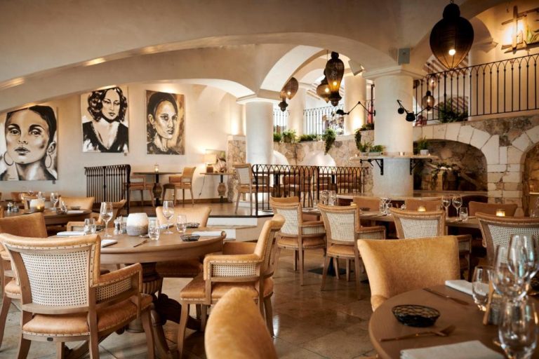 Elegante restaurante interior del Hotel U Capu Biancu con arcos de piedra, cuadros artísticos y mesas decoradas
