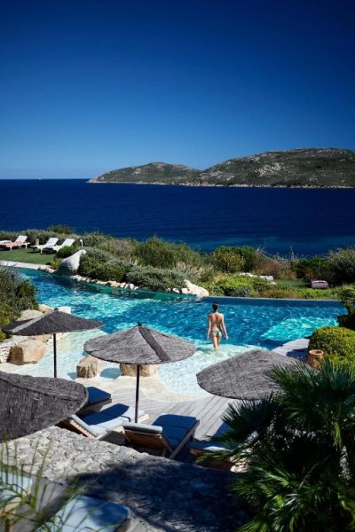 Piscina infinita con vistas al mar mediterráneo y sombrillas de paja en el Hotel U Capu Biancu