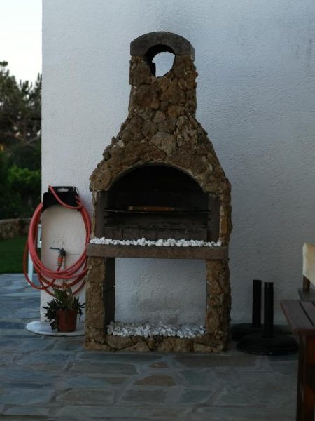 Barbacoa de piedra natural en exterior del Hotel Ilios and Irene con parrilla y chimenea tradicional