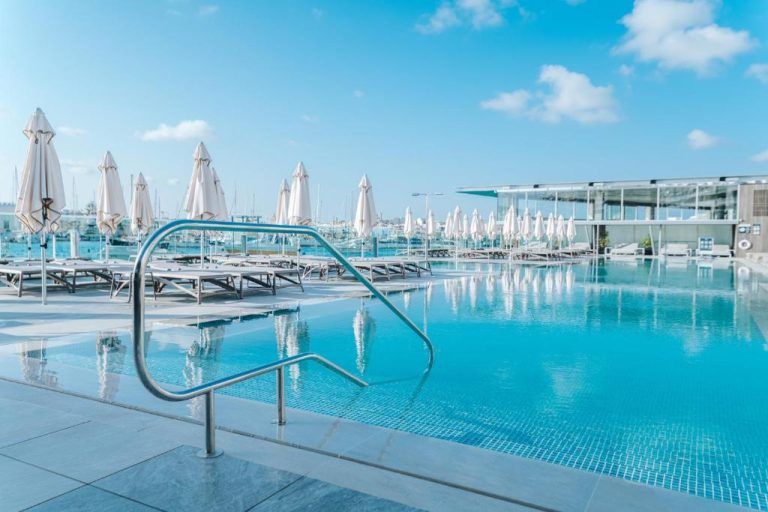 Piscina exterior con tumbonas y sombrillas blancas del Azur Hotel by ST Hotels con vistas al puerto
