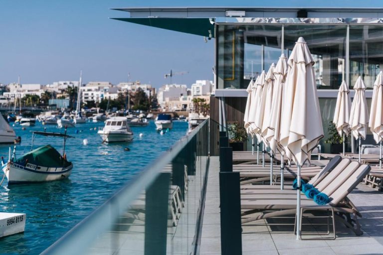 Terraza con tumbonas y sombrillas del Azur Hotel by ST Hotels con vistas al puerto deportivo de Malta