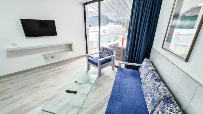 Salón con sofá azul, televisión y acceso directo a la piscina en Apartamentos Monte Verde