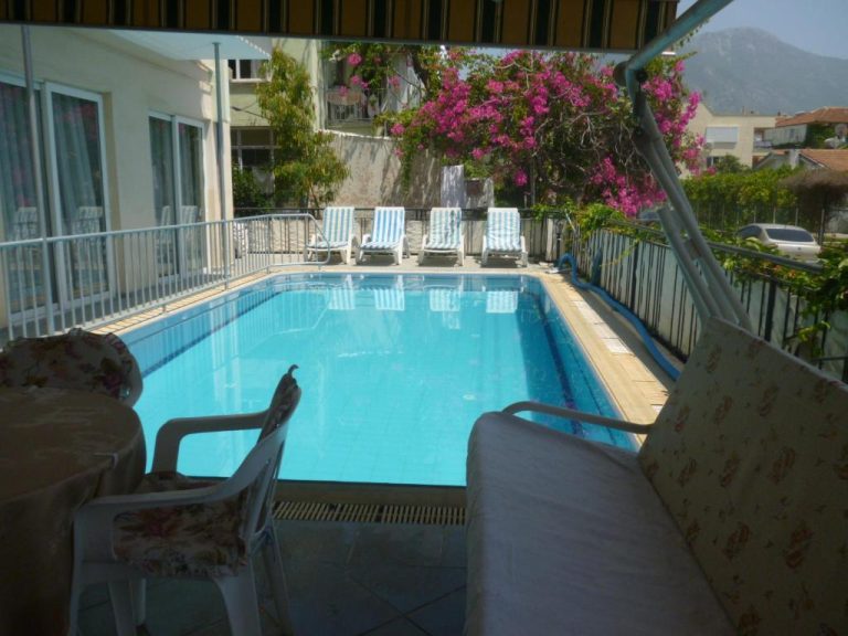 Piscina exterior con tumbonas y terraza del Cicek Hotel & Apartments rodeada de vegetación y montañas