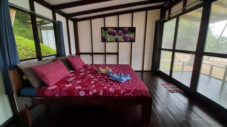 Habitación doble con suelo de madera y cama roja en Duli Beach Resort con vistas al jardín