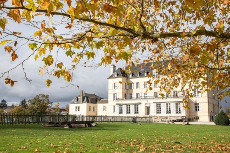 Fachada exterior del Château de Saulon rodeada de jardines en otoño con árboles de hojas doradas