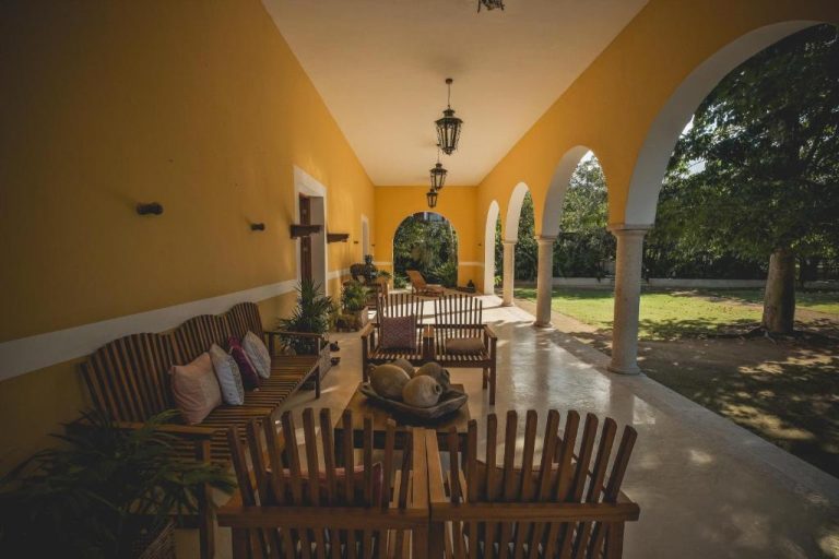 Terraza porticada colonial con sillones de madera y arcos blancos en Wakax Hacienda Boutique Hotel