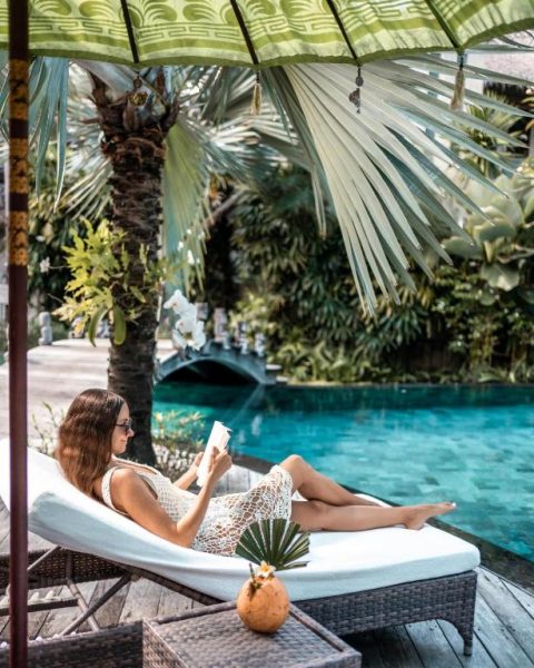 Mujer leyendo en tumbona junto a la piscina tropical del Blue Karma Dijiwa Seminyak en Bali
