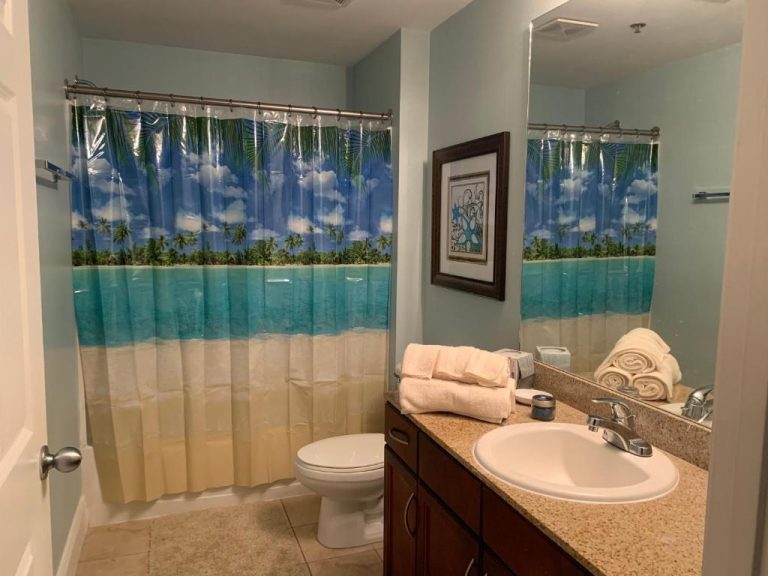 Baño completo con cortina de ducha tropical en apartamento Laketown Wharf, con lavabo y toallas
