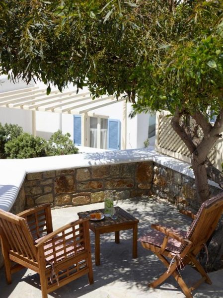 Terraza exterior con sillas de madera y mesa bajo árbol en Vencia Boutique Hotel, Mykonos