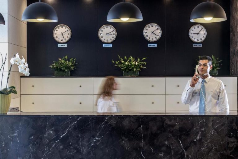 Recepción de mármol del Aeolos Beach Resort con relojes de ciudades del mundo y personal atendiendo