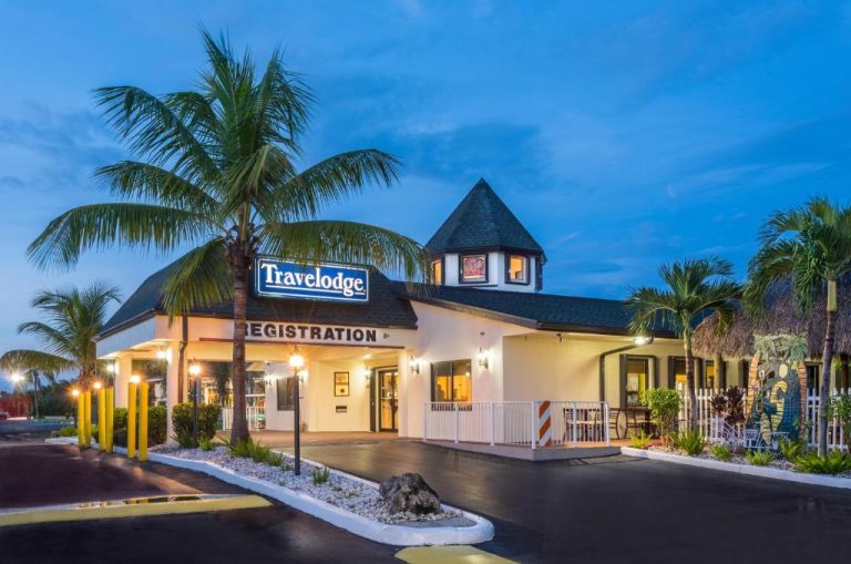 Fachada exterior iluminada del Travelodge Florida City Everglades con palmeras y área de registro