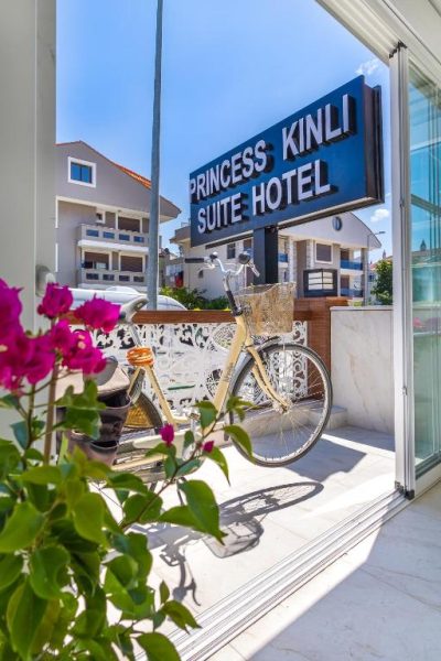 Entrada del Princess Kinli Suite Hotel con bicicleta decorativa y flores de buganvilla en primer plano