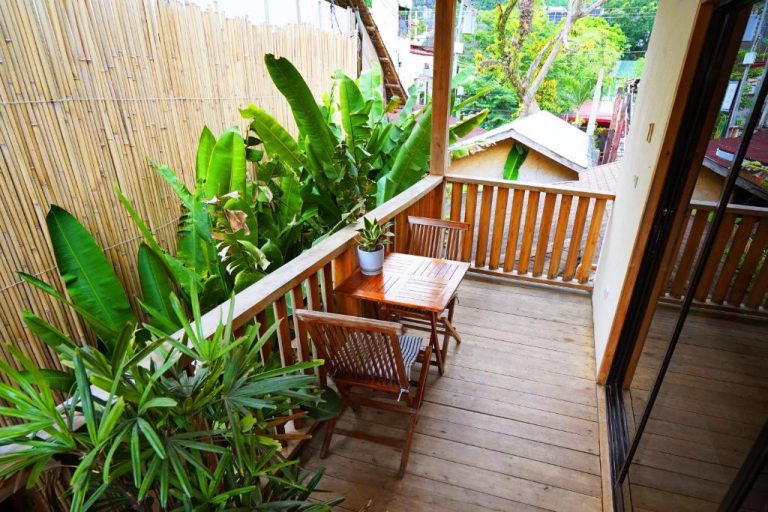 Terraza de madera con mesa y sillas en Fisheye The Rooms, rodeada de plantas tropicales