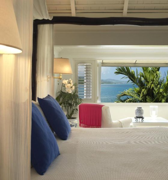 Habitación con dosel y cojines azules con vista al mar turquesa en Round Hill Hotel & Villas Jamaica