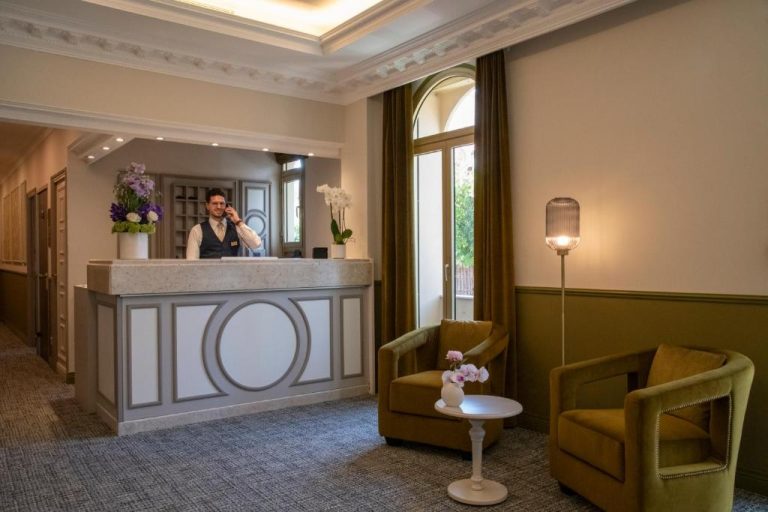 Recepción elegante del Hôtel Petit Palais con conserje atendiendo y zona de espera con sillones verdes
