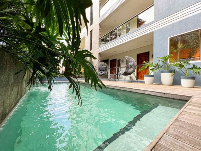 Piscina exterior con terraza de madera y vegetación tropical del Bill Tourist Inn