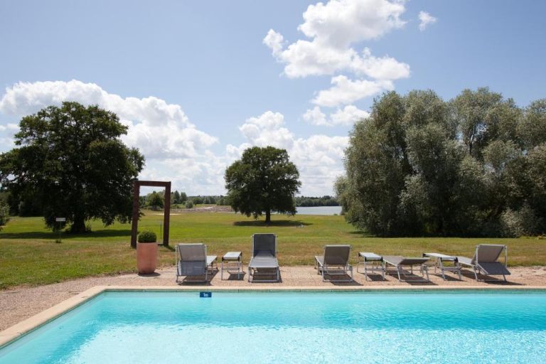 Piscina exterior con tumbonas y vistas al lago y jardines del Hotel Le Noirlac en Francia