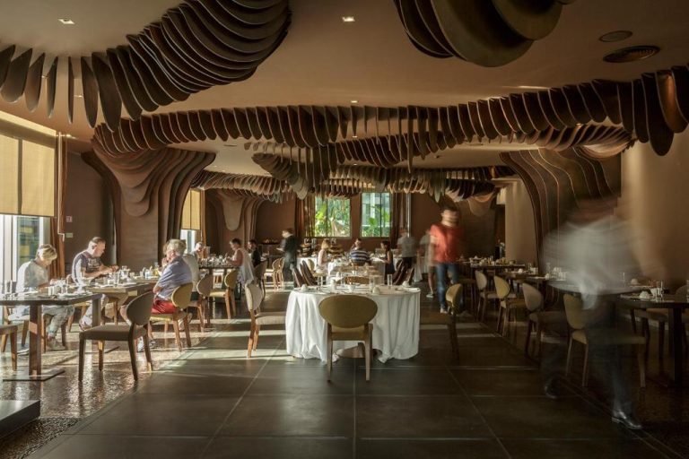 Restaurante del The Vine Hotel con espectacular techo ondulado de madera y mesas elegantemente decoradas