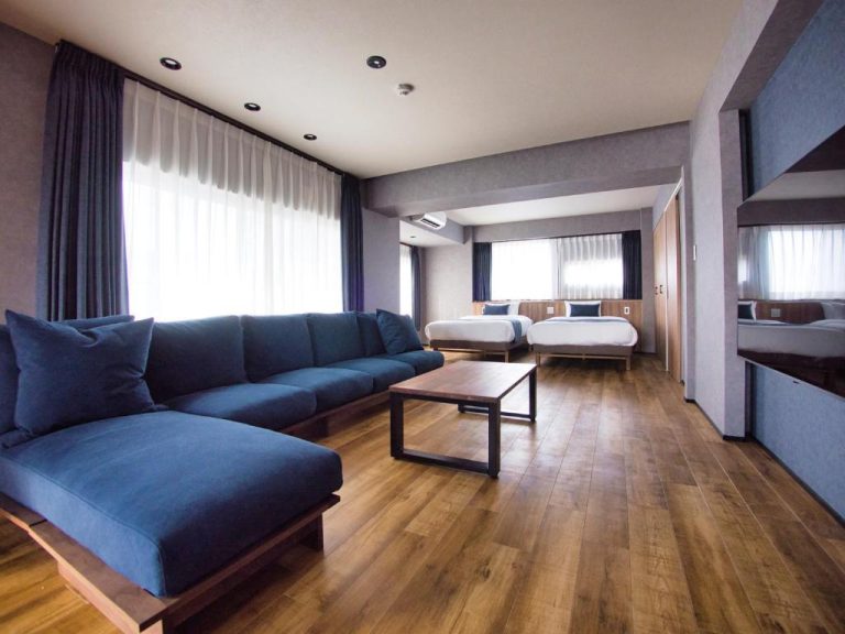 Suite amplia del hotel Ulu Tokyo con sofá azul, suelo de madera y dos camas dobles al fondo