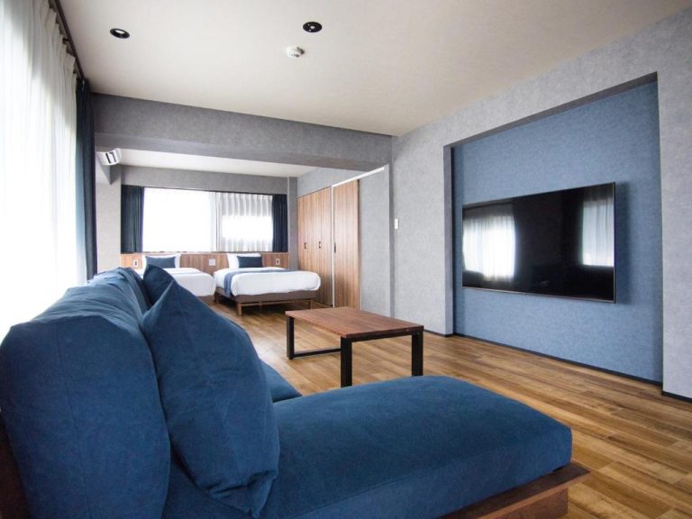 Suite del hotel Ulu Tokyo con sofá azul, cama doble y televisión de pantalla plana en la pared