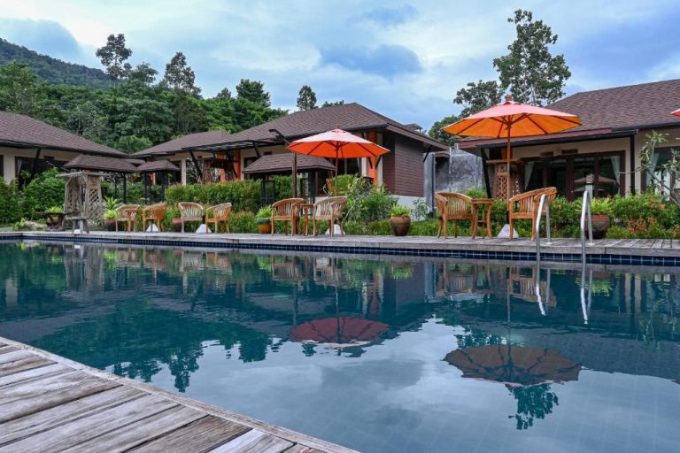 Piscina exterior con tumbonas y sombrillas naranjas rodeada de bungalows y jardín tropical en Cascade Tara