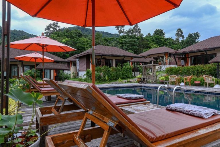 Piscina exterior con tumbonas y sombrillas rojas rodeada de bungalows tropicales en Cascade Tara